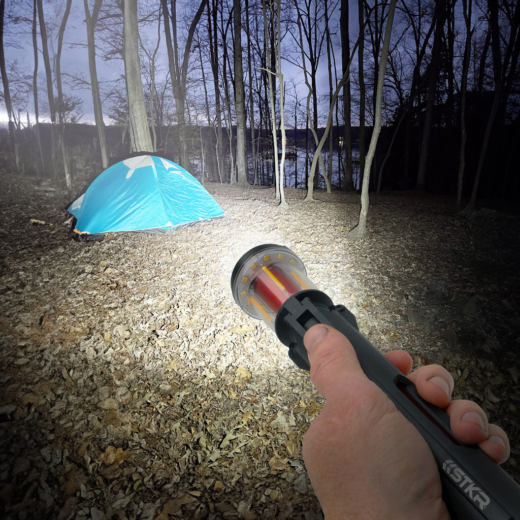 Person holding a FLi-MORPHE flashlight in a forest with a blue tent in the background