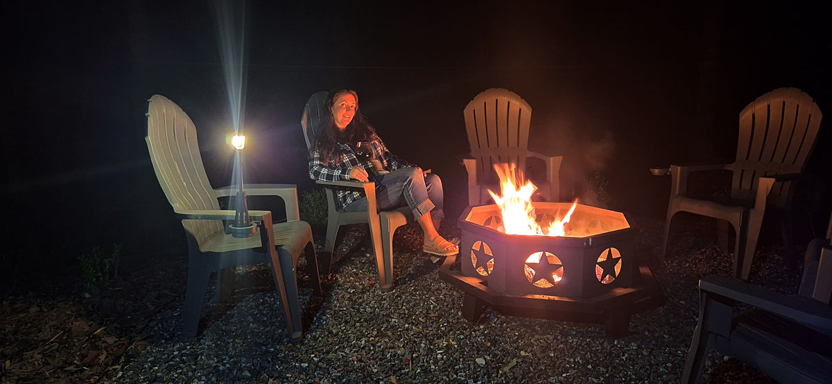 Person sitting by a fire pit at night with Adirondack chairs around.