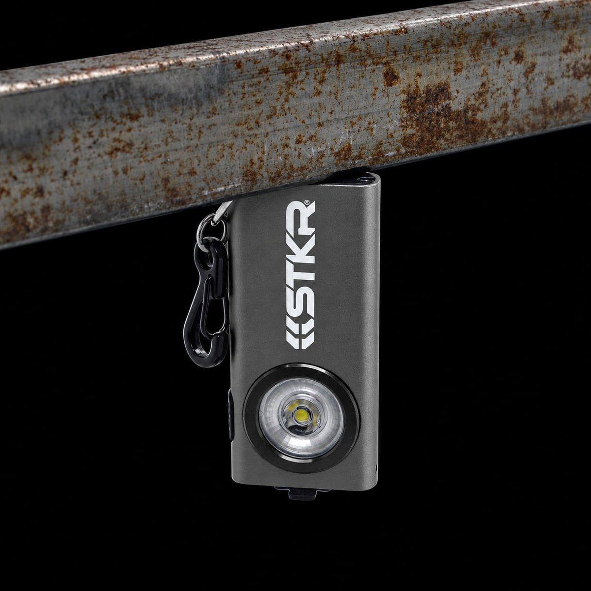 Gray STKR SlimJIMMY keychain light held by its magnetic base under a rusty steel bar