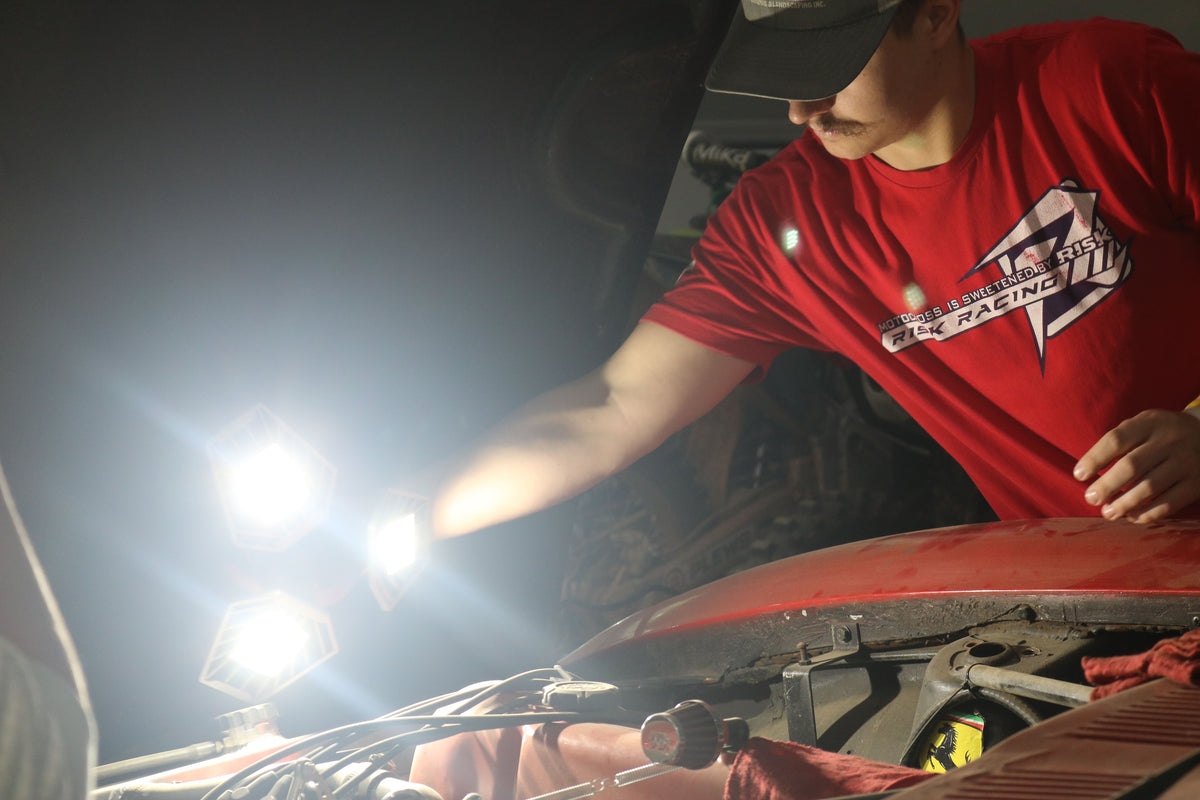Person in a red racing shirt working on a vehicle at night lighting the engine bay with a TRiLIGHT Shoplight V2.